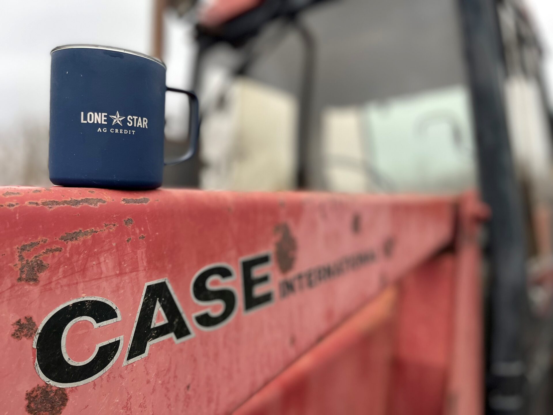 Navy blue AgTrust Farm Credit mug sitting on a red Case tractor