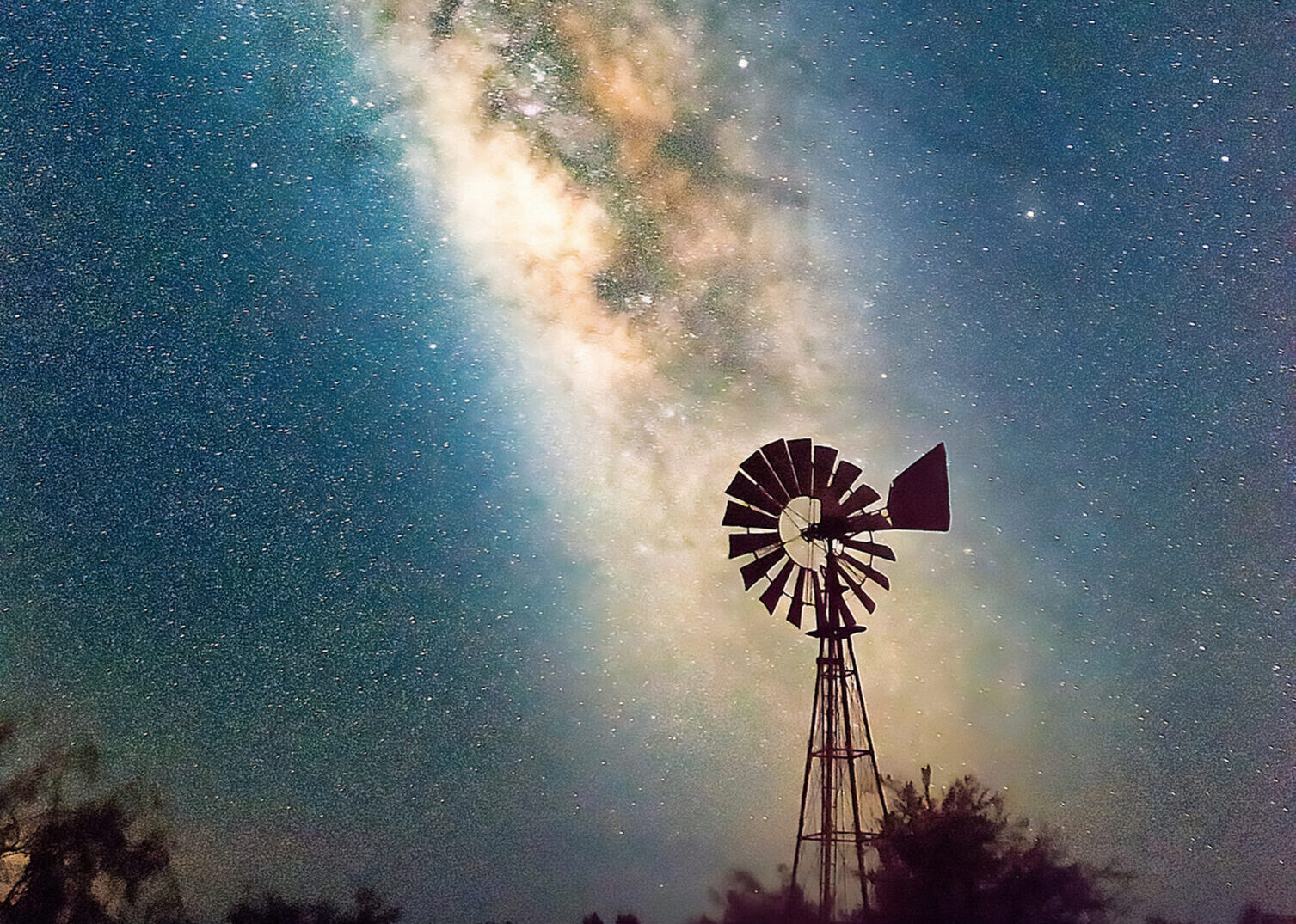 Silhouette of a windmill against a vibrant starry night sky.