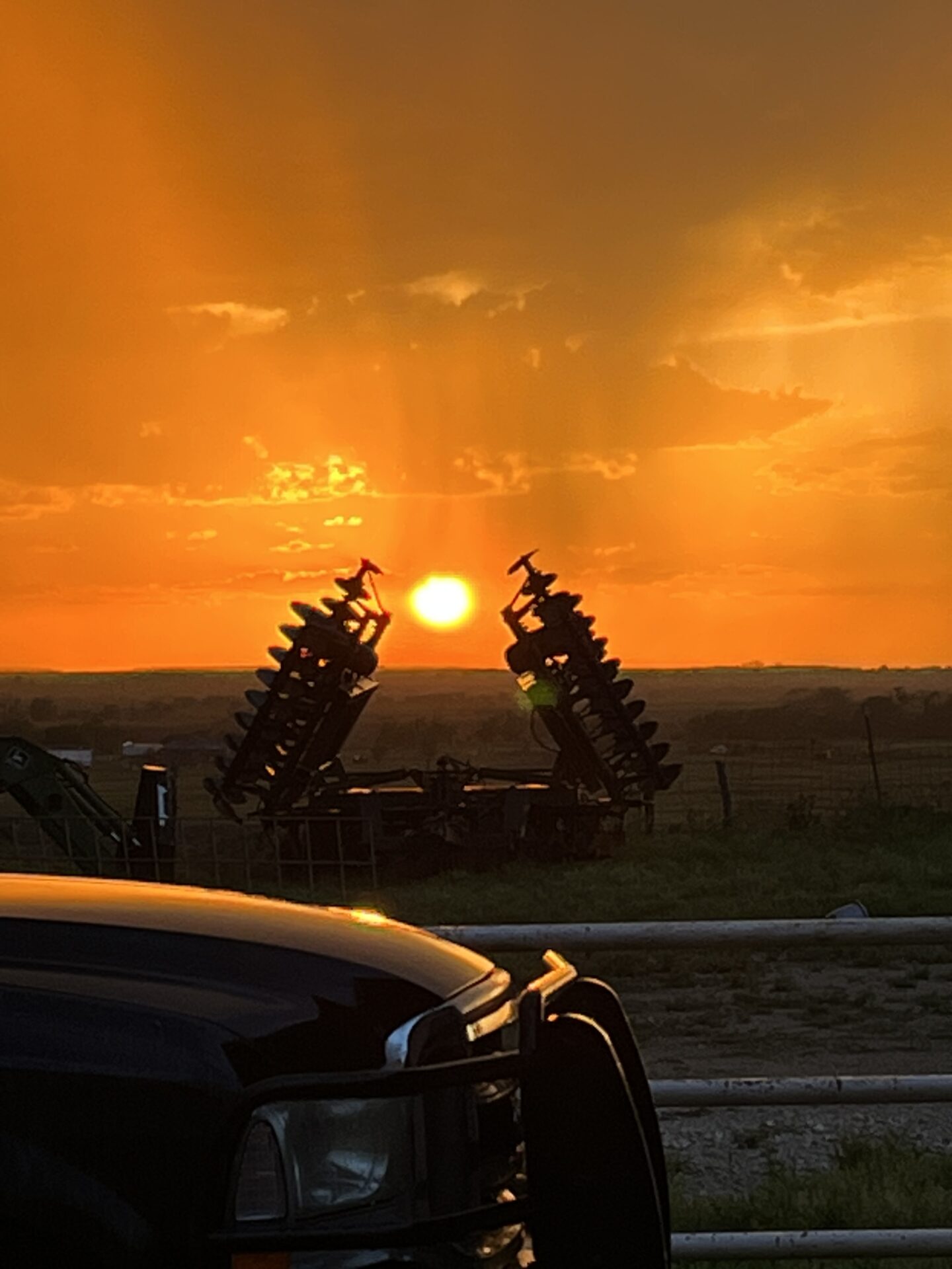 Plow implement in silhouette with a bright orange sunset.