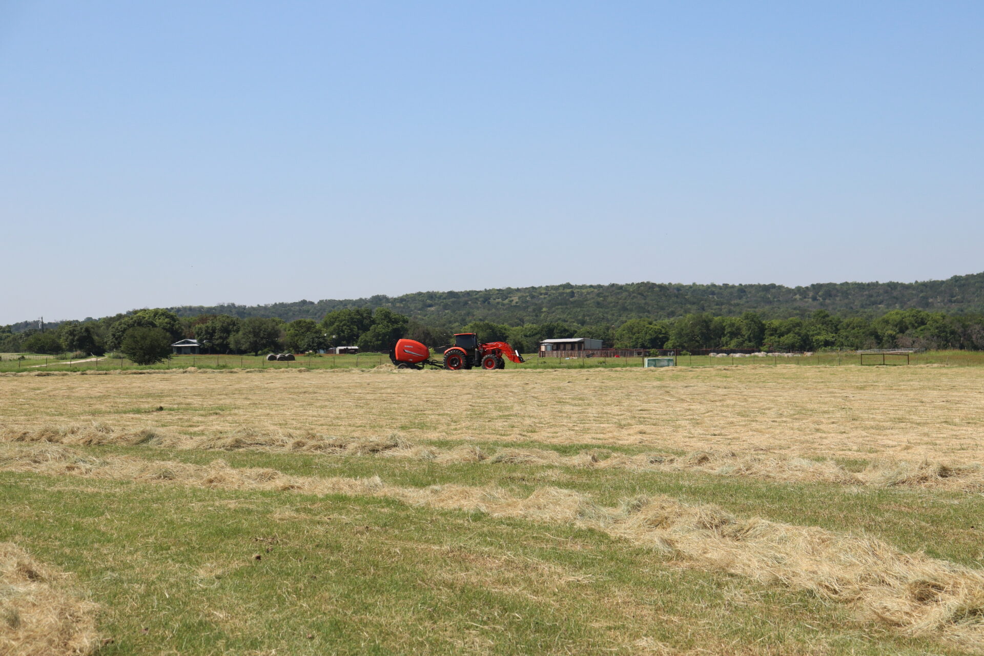 Red tractor baling hay in pasture
