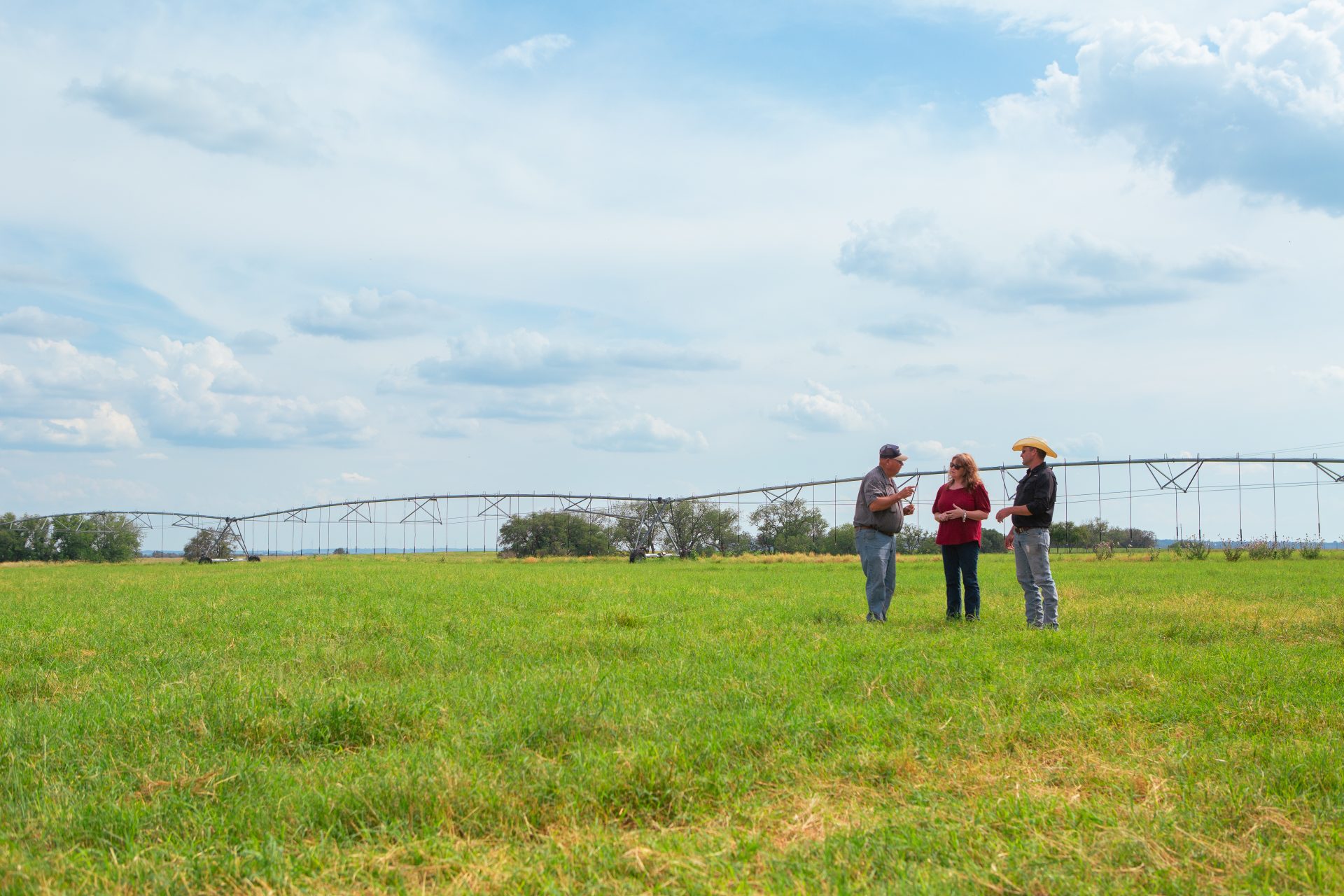 Two men and a woman talking in a green pasture with an irrigation pivot in the background.