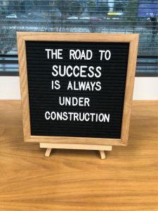 Sign on a desk that says, "The road to success is always under construction".
